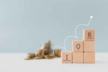 ROI text, abbreviation of Return On Investment, on wooden cube blocks with jump arrow and blurred money coin stack including copy space - obrazy, fototapety, plakaty