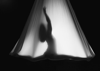 Fly yoga. Girl in a white hammock on a black background shows aerial acrobatics. Gymnastics,...