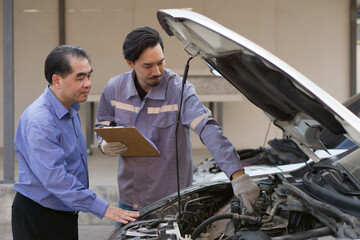 Two guys are standing by a car with the hood open, staring at the engine inside.