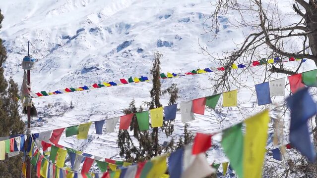 Slow motion shot of prayer flags waving in the wind in front of snowy Himalayan mountain peaks during the winter season as seen from Shashur Monastery in Keylong at Lahaul Valley in Himachal Pradesh.