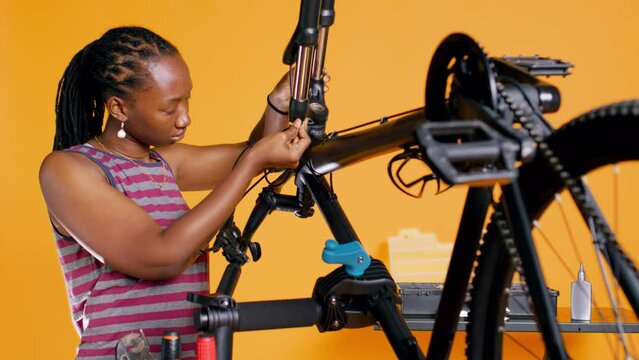 BIPOC technician uses screwdriver to unmount bicycle handlebars, testing components quality in studio background atelier shop. Specialist mechanic unscrewing bike parts in order to mend them, camera B