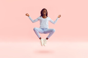 Fototapeta na wymiar Full body portrait of a young smiling happy african american woman in casual clothes holding spreading hands doing yoga exercise and meditating with closed eyes isolated on a studio pink background.