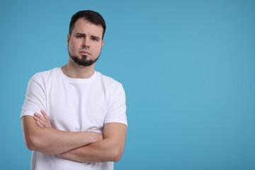 Portrait of sad man with crossed arms on light blue background, space for text