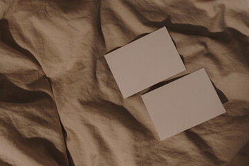 Blank paper card sheets with copy space on wrinkled bed blanket cloth with aesthetic warm sunlight...