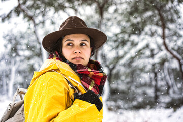 Fototapeta premium Young woman with yellow rain coat hiking in the forset on a snowy day