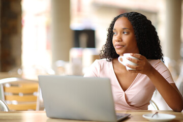 Black woman in a bar with a laptop drinking and looking away
