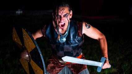Viking warrior shouting during battle with black war paint, openig his mouth and holding his sword.