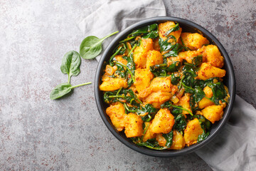 Saag aloo is a classic Indian style side dish featuring potatoes fried in spices and spinach closeup on the bowl on the table. Horizontal top view from above - obrazy, fototapety, plakaty