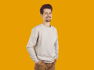 Confident handsome young man standing with his hands in pockets. Portrait of cheerful attractive guy in beige pullover posing against yellow background in studio © Studio Romantic