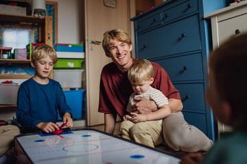 Dad with three sons playing in kids room, air hockey. Concept of Father's Day, and fatherly love....