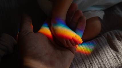 A man holds his newborn son by the leg. Beam of light through a prism. 