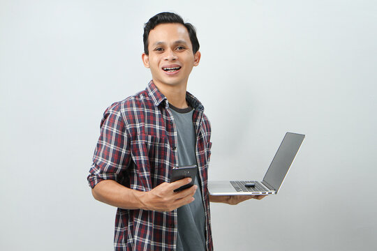 Happy Asian Indonesian Man Holding Smartphone And Laptop Computer On Isolated Background