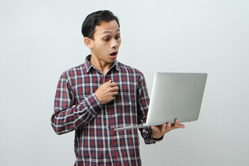 Shocked and wow expression of asian indonesian man holding laptop computer on isolated background