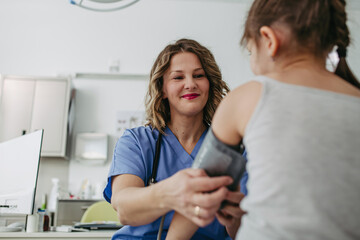 Doctor examining young girl, measuring blood pressure, using medical blood pressure monitor....