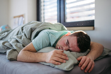 Young man with down syndrome sleeping in his bed. Lying on abdomen, resting in bedroom.