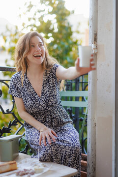 Smiling woman giving glass and sitting in balcony