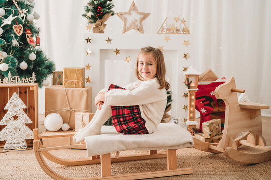 Smiling girl sitting on sled near Christmas decoration at home