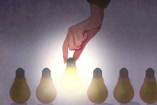 Hand choosing light bulb from row of unlit bulbs