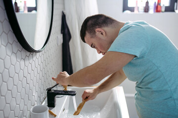 Young man with down syndrome in bathroom, cleaning comb, rinsing it in the water.
