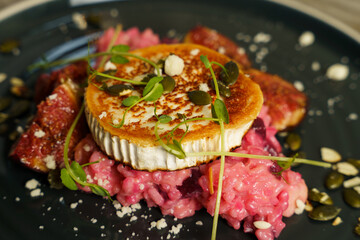 Risotto with beetroot, grilled goat cheese, fig and toasted pumpkin seeds on wooden table