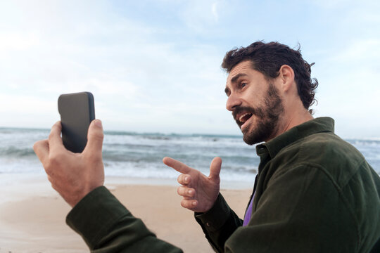 Man gesturing and talking on video call through mobile phone at beach