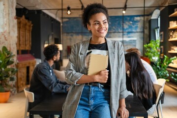 Successful businesswoman standing in creative office. Young woman entrepreneur in a coworking space smiling