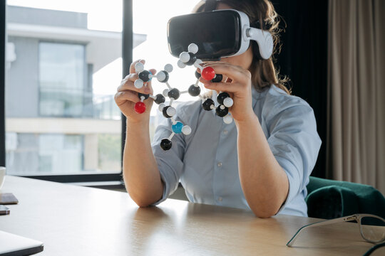 Scientist wearing virtual reality headset and holding molecular structure at desk