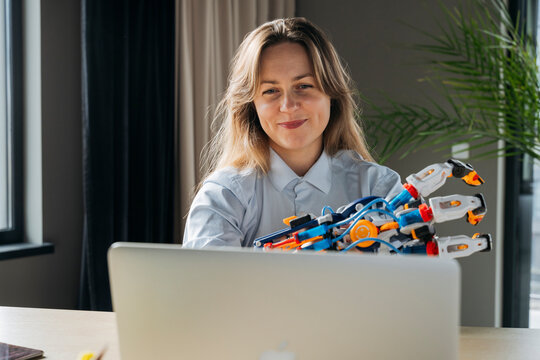 Smiling engineer showing robot arm project on video call through laptop in office
