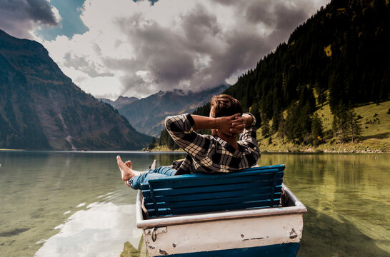 Young man sitting in boat at lake Vilsalpsee near mountains, Tyrol, Austria