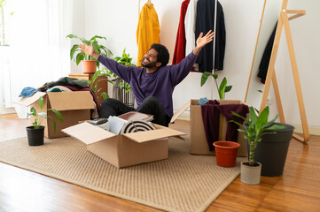 Cheerful young man with arms raised organizing and decluttering at home