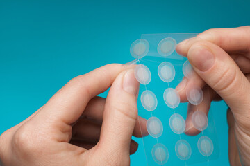 Close-up round acne patch on finger on blue background. Acne patches for treatment of pimple and...