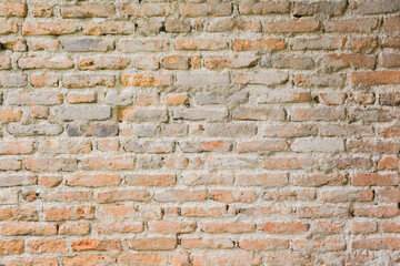 The textured background of an old red brick wall has cracks of loose plaster.