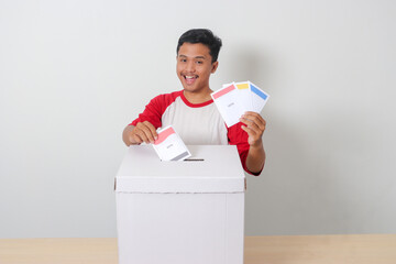 Portrait of excited Asian man inserting and putting the voting paper into the ballot box. General...