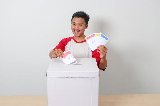 Portrait of excited Asian man inserting and putting the voting paper into the ballot box. General elections or Pemilu for the president and government of Indonesia. Isolated image on white background