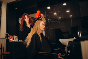 Master woman hairdresser dries the girl's hair with a hairdryer after washing in a beauty salon.