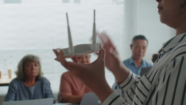 Back view of female tutor holding Wi-Fi router while giving lesson to group of seniors