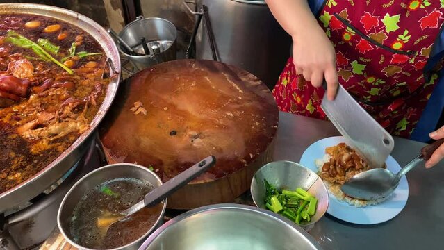 Giant pan of Khao Kha Moo, braised stew pork leg on rice and Chinese broccoli, is seen as the chef prepares the traditional Thai dish at a street food stall in Bangkok, Thailand.