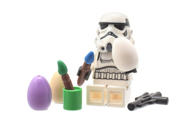 Obraz premium Lego minifigure of warrior Star Wars as artist is painting an easter egg isolated on white. Editorial illustrative image of popular plastic toy constructor.