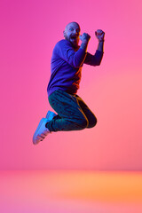 Full-length image of bearded bald man in casual clothes emotionally jumping against pink background...