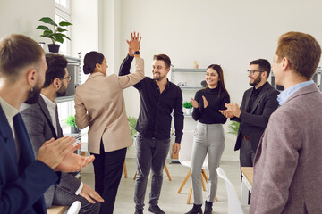 Friendly colleagues give high fives congratulating each other on business achievements and excellent results at work. People applaud their colleagues during meeting in office. Concept of team success.