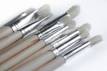 Fototapeta premium Paint brushes lie diagonally on one off-white background. Narrow depth of field