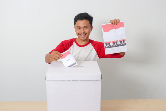Portrait of excited Asian man inserting and putting the voting paper into the ballot box. General elections or Pemilu for the president and government of Indonesia. Isolated image on white background