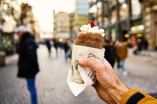 Tourist holds trdelnik against Prague street, Grilled rolled dough topped with sugar, Traditional Czech hot sweet pastry, street bakery in Prague