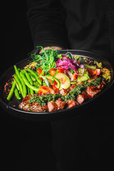 Men's waiter hands hold a Roastbeef salad with vegetables on plate