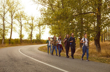Obraz premium Team of hiking friends embarks on a journey, walking together along a nature trail. Camaraderie is evident as they traverse the road, creating memories during this joyous group hiking trip.