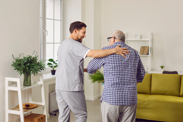 Portrait of a young nurse helping a grey-haired senior patient to walk at home. Physiotherapist...