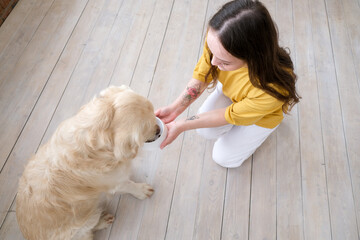 Portrait of happy young woman with pet dog, sitting on floor at home. Caucasian female hugging golden retriever in living room