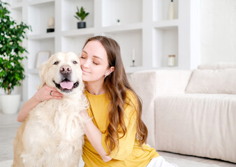 Portrait of happy young woman with pet dog, sitting on floor at home. Caucasian female hugging golden retriever in living room