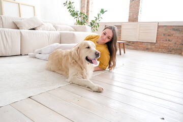 Portrait of happy young woman with pet dog, sitting on floor at home. Caucasian female hugging...