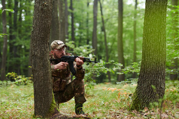 An elite soldier, camouflaged and stealthily navigating through dangerous woodland terrain,...